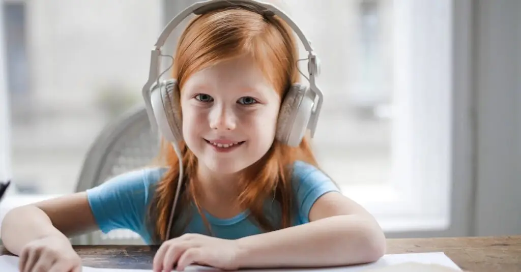A cheerful red-haired girl listening to music with headphones while drawing indoors.