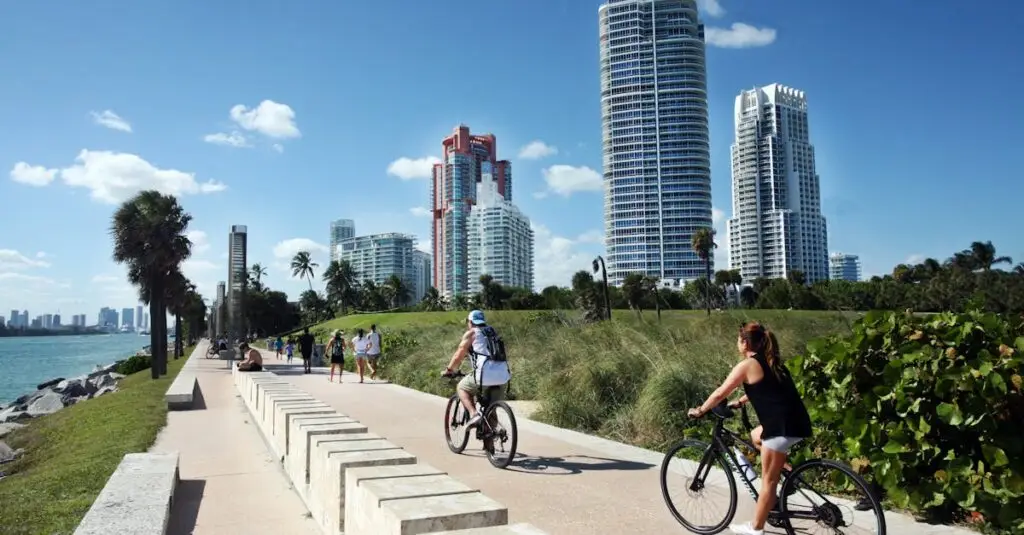 Cyclists ride along a scenic path in Miami Beach, with skyscrapers in the background.
